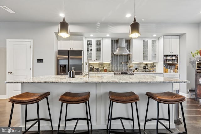 kitchen with a large island, white cabinets, stainless steel appliances, and wall chimney range hood