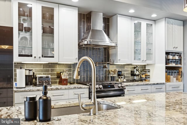 kitchen with wall chimney exhaust hood, light stone countertops, white cabinetry, and tasteful backsplash