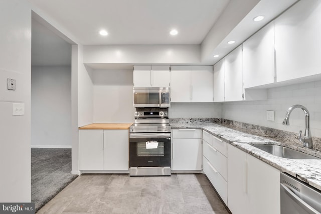 kitchen featuring light stone countertops, white cabinetry, sink, stainless steel appliances, and decorative backsplash