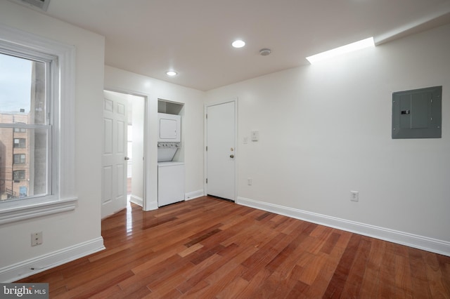 unfurnished room with stacked washer / dryer, a healthy amount of sunlight, electric panel, and hardwood / wood-style floors