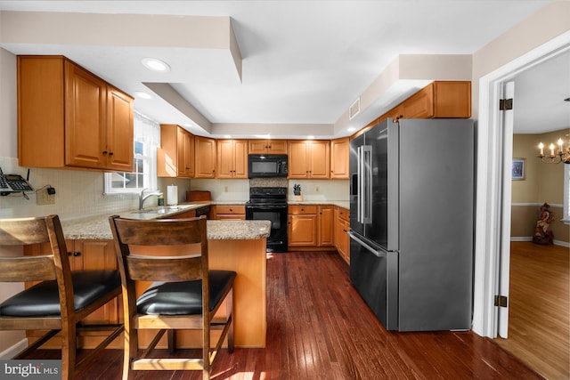 kitchen featuring black appliances, tasteful backsplash, a peninsula, and dark wood finished floors