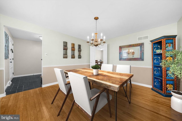 dining room featuring baseboards, wood finished floors, visible vents, and a notable chandelier