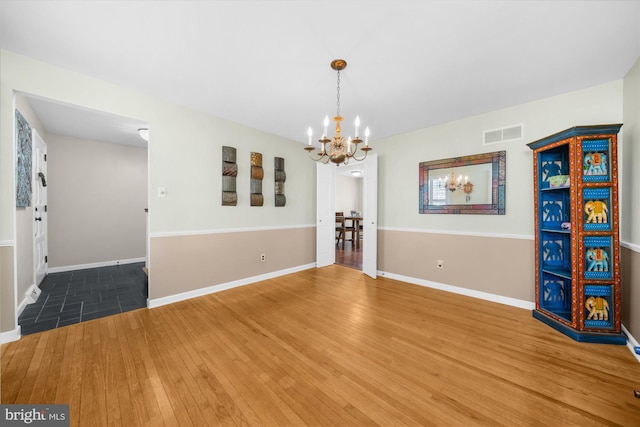 unfurnished dining area with hardwood / wood-style floors, baseboards, visible vents, and a notable chandelier