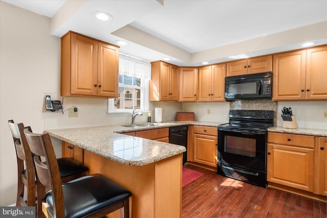 kitchen featuring a breakfast bar, a peninsula, light stone countertops, black appliances, and a sink