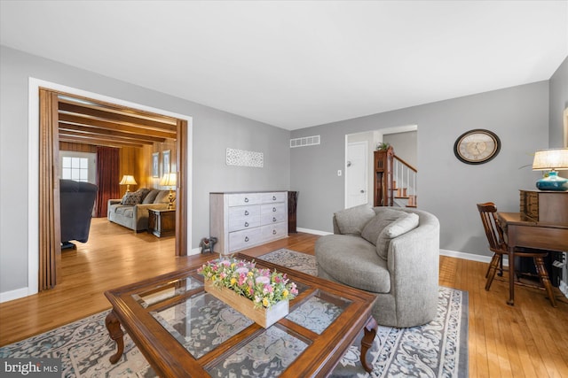 living room featuring wood finished floors, visible vents, baseboards, and stairs