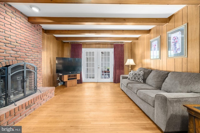 living room featuring wood walls, french doors, light wood-type flooring, a brick fireplace, and beamed ceiling