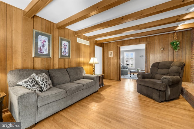 living area with light wood finished floors, visible vents, beamed ceiling, and wood walls