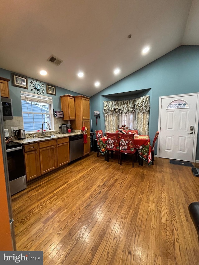 kitchen featuring sink, light hardwood / wood-style floors, vaulted ceiling, and appliances with stainless steel finishes