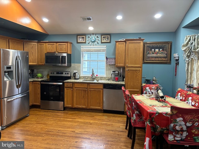 kitchen with sink, stainless steel appliances, vaulted ceiling, and light hardwood / wood-style flooring