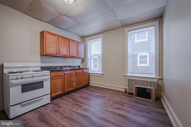 kitchen with radiator heating unit, a drop ceiling, white range oven, and hardwood / wood-style flooring