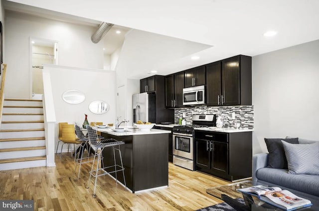 kitchen with a kitchen bar, appliances with stainless steel finishes, tasteful backsplash, light hardwood / wood-style flooring, and an island with sink