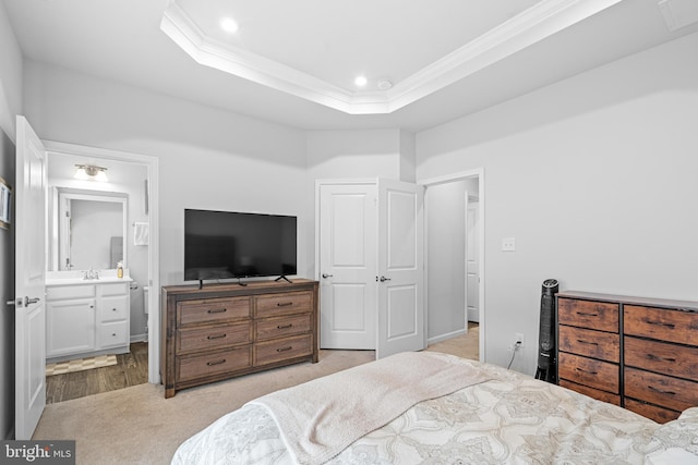 bedroom with light colored carpet, connected bathroom, a tray ceiling, and ornamental molding