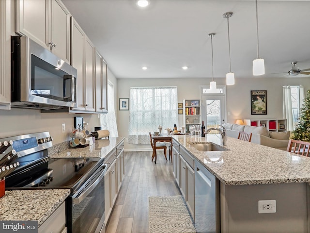 kitchen with sink, stainless steel appliances, light hardwood / wood-style flooring, an island with sink, and decorative light fixtures