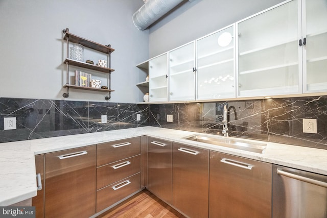 kitchen featuring light hardwood / wood-style floors, light stone countertops, sink, stainless steel dishwasher, and backsplash