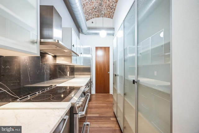 kitchen featuring dark wood-type flooring, brick ceiling, wall chimney range hood, stainless steel electric range, and backsplash