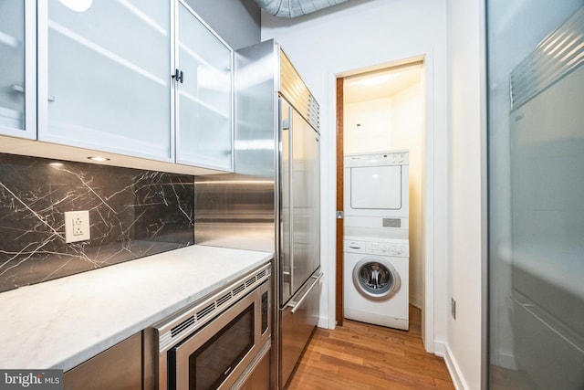 kitchen with built in appliances, backsplash, stacked washer / dryer, and light hardwood / wood-style floors