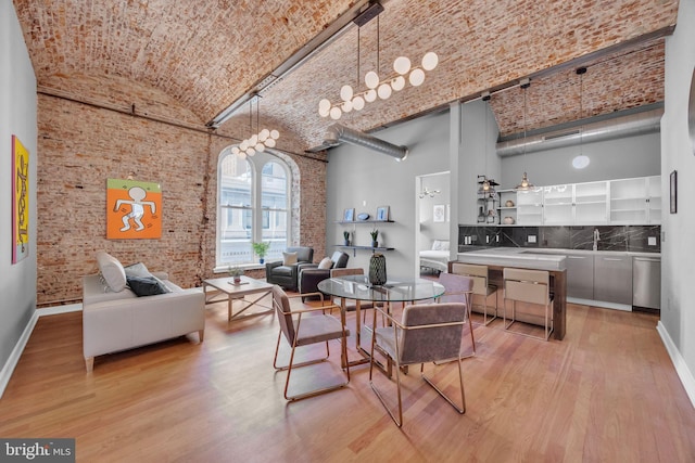 dining space featuring brick ceiling, light wood-type flooring, high vaulted ceiling, and brick wall