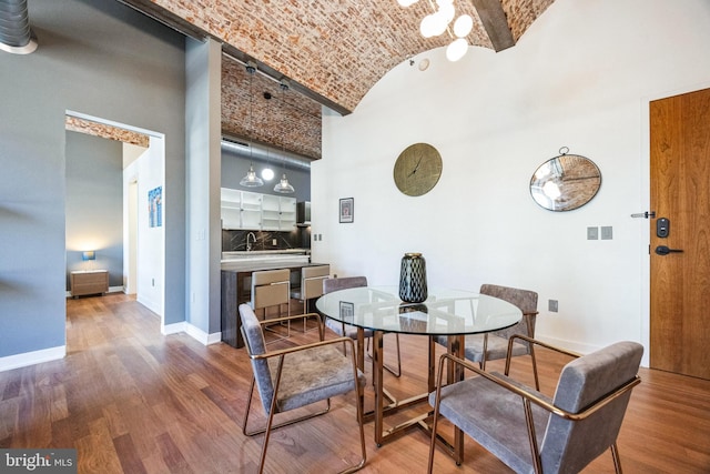 dining room with sink, brick ceiling, hardwood / wood-style floors, and vaulted ceiling