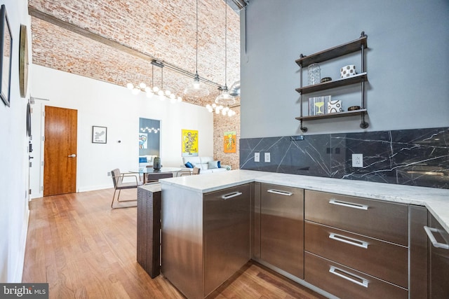 kitchen featuring light stone counters, kitchen peninsula, light hardwood / wood-style flooring, decorative backsplash, and a towering ceiling