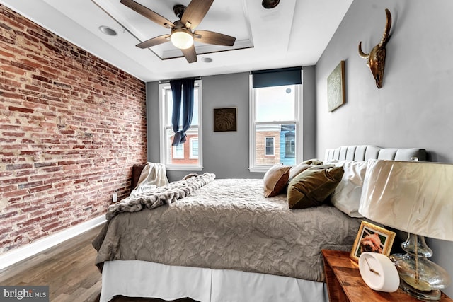 bedroom featuring wood-type flooring, a tray ceiling, ceiling fan, and brick wall