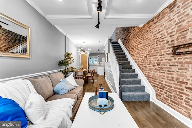 living room with dark hardwood / wood-style flooring, ornamental molding, brick wall, and an inviting chandelier