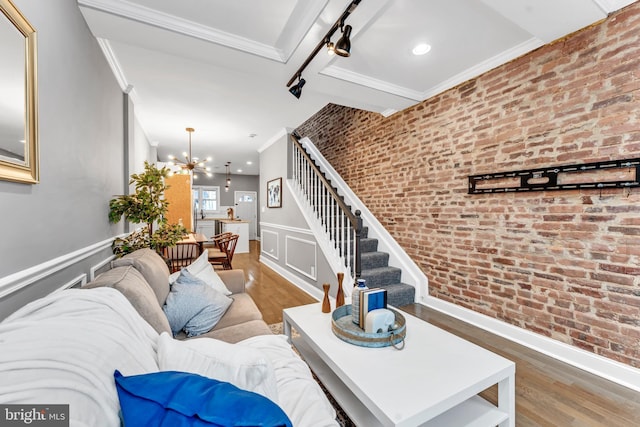 living room featuring crown molding, an inviting chandelier, brick wall, and hardwood / wood-style flooring