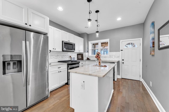 kitchen featuring light stone countertops, white cabinetry, a center island, stainless steel appliances, and decorative light fixtures