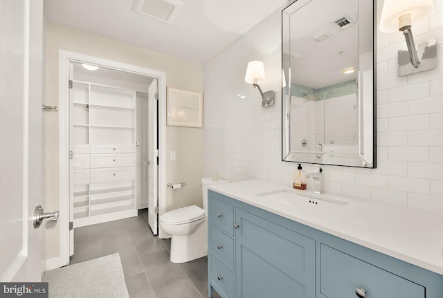 bathroom featuring a tile shower, vanity, toilet, and tile walls