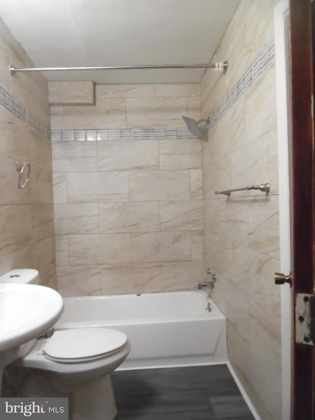 bathroom featuring wood-type flooring, tiled shower / bath combo, and toilet