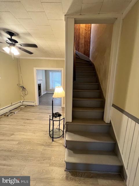 stairs featuring hardwood / wood-style floors, ceiling fan, ornamental molding, and a baseboard heating unit