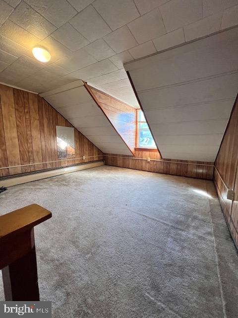 bonus room with carpet, vaulted ceiling, a baseboard heating unit, and wood walls