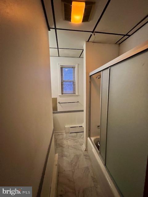 bathroom with bath / shower combo with glass door and a baseboard heating unit