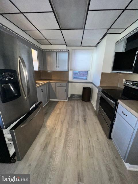 kitchen featuring stainless steel appliances, a drop ceiling, light hardwood / wood-style floors, and gray cabinetry