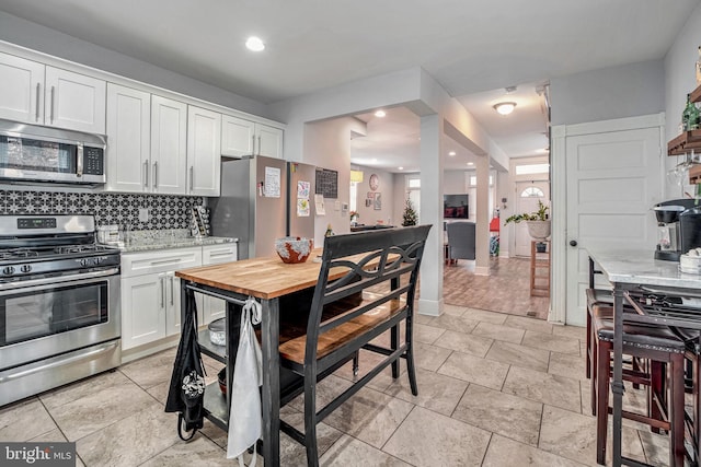 kitchen with backsplash, light stone counters, white cabinets, and appliances with stainless steel finishes