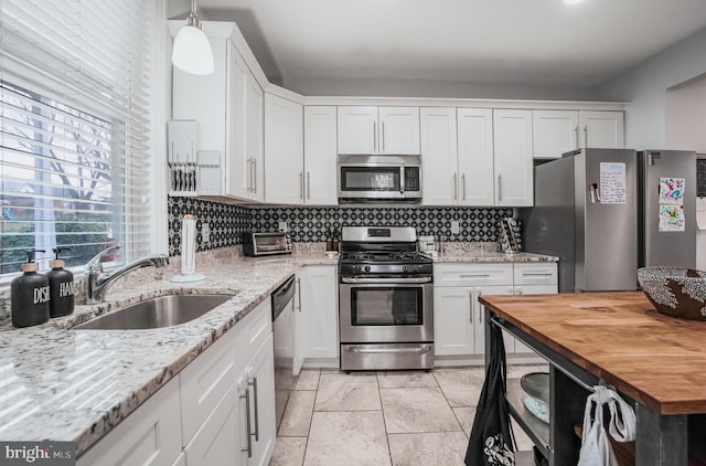 kitchen with white cabinetry, sink, stainless steel appliances, decorative light fixtures, and decorative backsplash