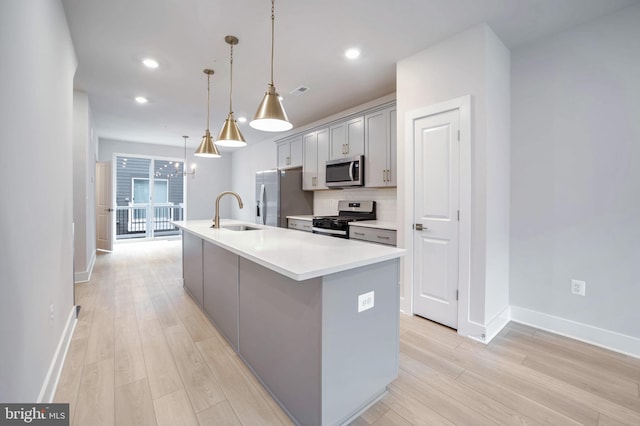 kitchen featuring gray cabinets, pendant lighting, sink, stainless steel appliances, and a center island with sink