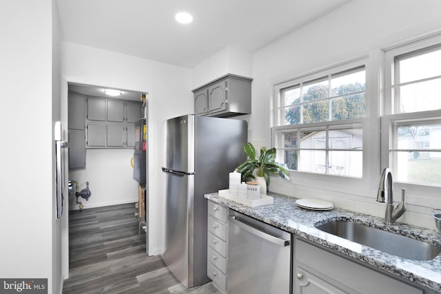 kitchen with appliances with stainless steel finishes, dark hardwood / wood-style flooring, light stone counters, sink, and gray cabinets