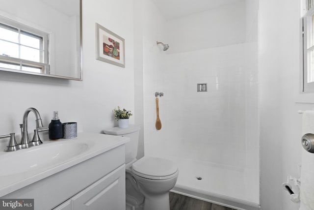 bathroom with tiled shower, hardwood / wood-style floors, vanity, and toilet