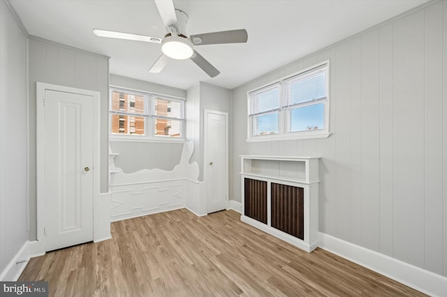 interior space featuring multiple windows, ceiling fan, wood walls, and light wood-type flooring