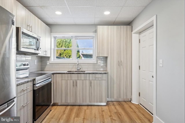 kitchen with a drop ceiling, sink, dark stone counters, light hardwood / wood-style floors, and appliances with stainless steel finishes