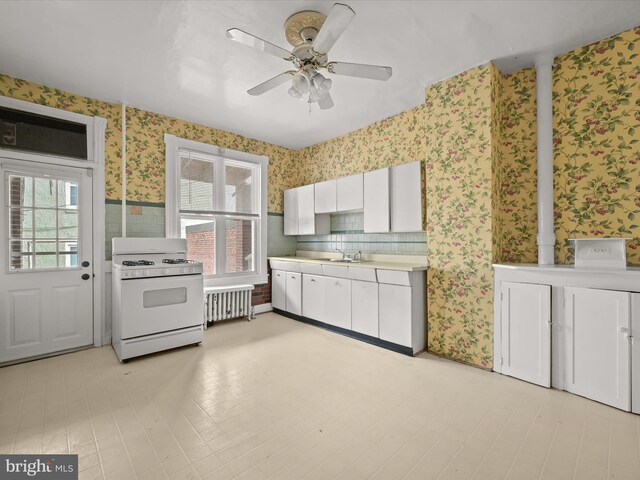 kitchen featuring white gas range oven, ceiling fan, sink, white cabinets, and radiator heating unit