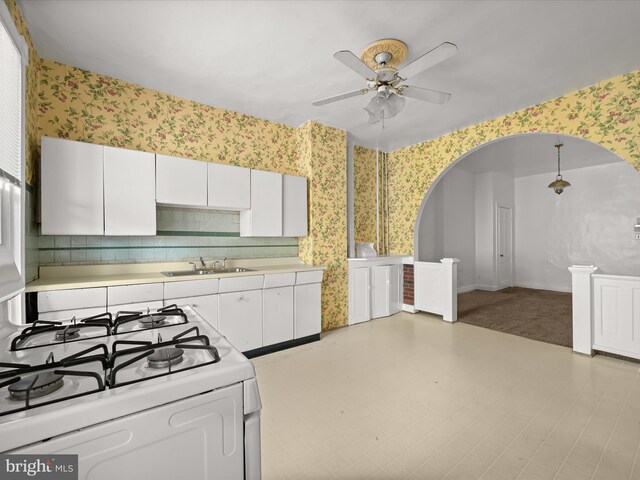 kitchen featuring light carpet, gas range gas stove, ceiling fan, sink, and white cabinets