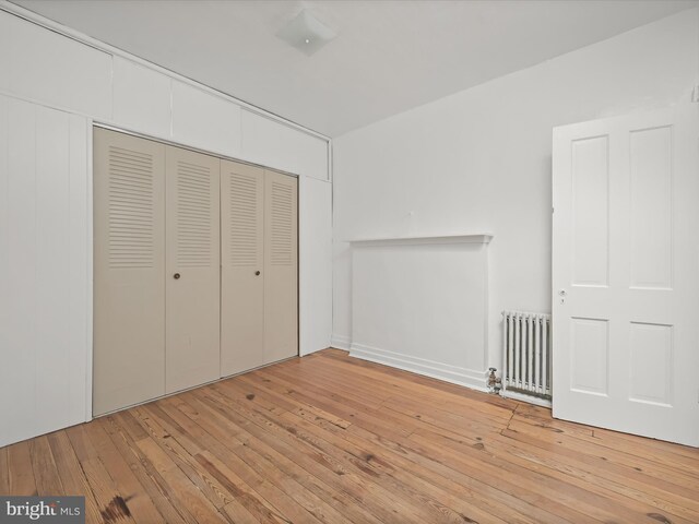 unfurnished bedroom featuring radiator heating unit, a closet, and wood-type flooring