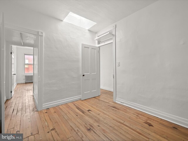 empty room with light wood-type flooring, radiator heating unit, and a skylight