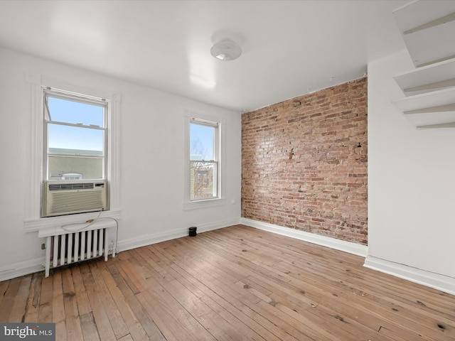 unfurnished room with light hardwood / wood-style flooring, plenty of natural light, radiator, and brick wall