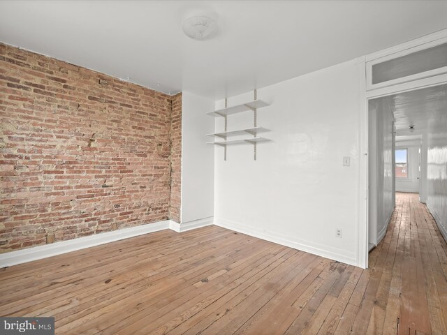 unfurnished dining area with wood-type flooring and brick wall