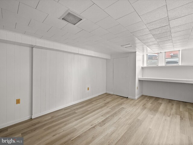 basement featuring light wood-type flooring and wooden walls