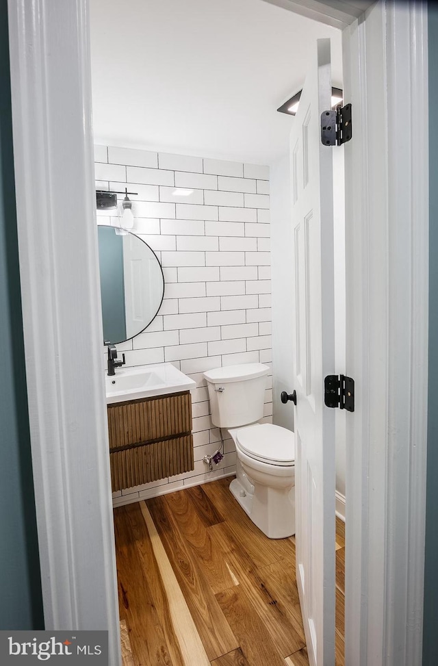 bathroom with hardwood / wood-style floors, vanity, tile walls, and toilet