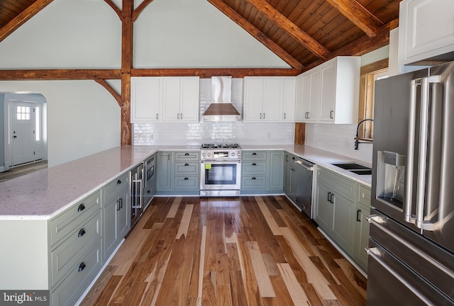 kitchen with wall chimney exhaust hood, vaulted ceiling with beams, kitchen peninsula, white cabinets, and high end appliances