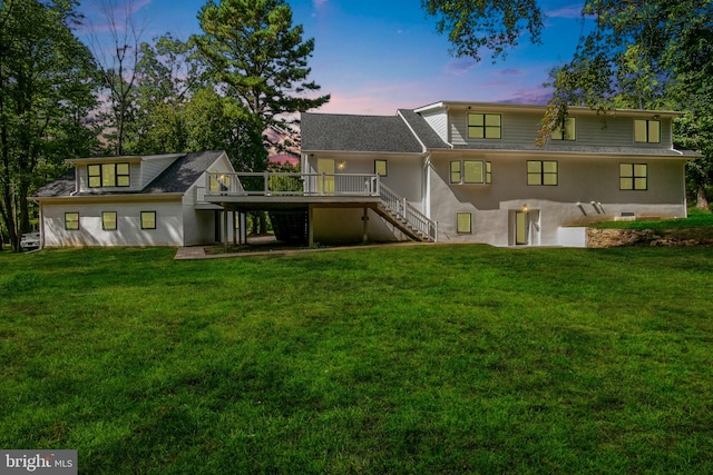 back house at dusk featuring a lawn and a wooden deck